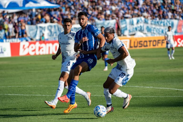 Three soccer players compete fiercely during an outdoor match on a sunny day.